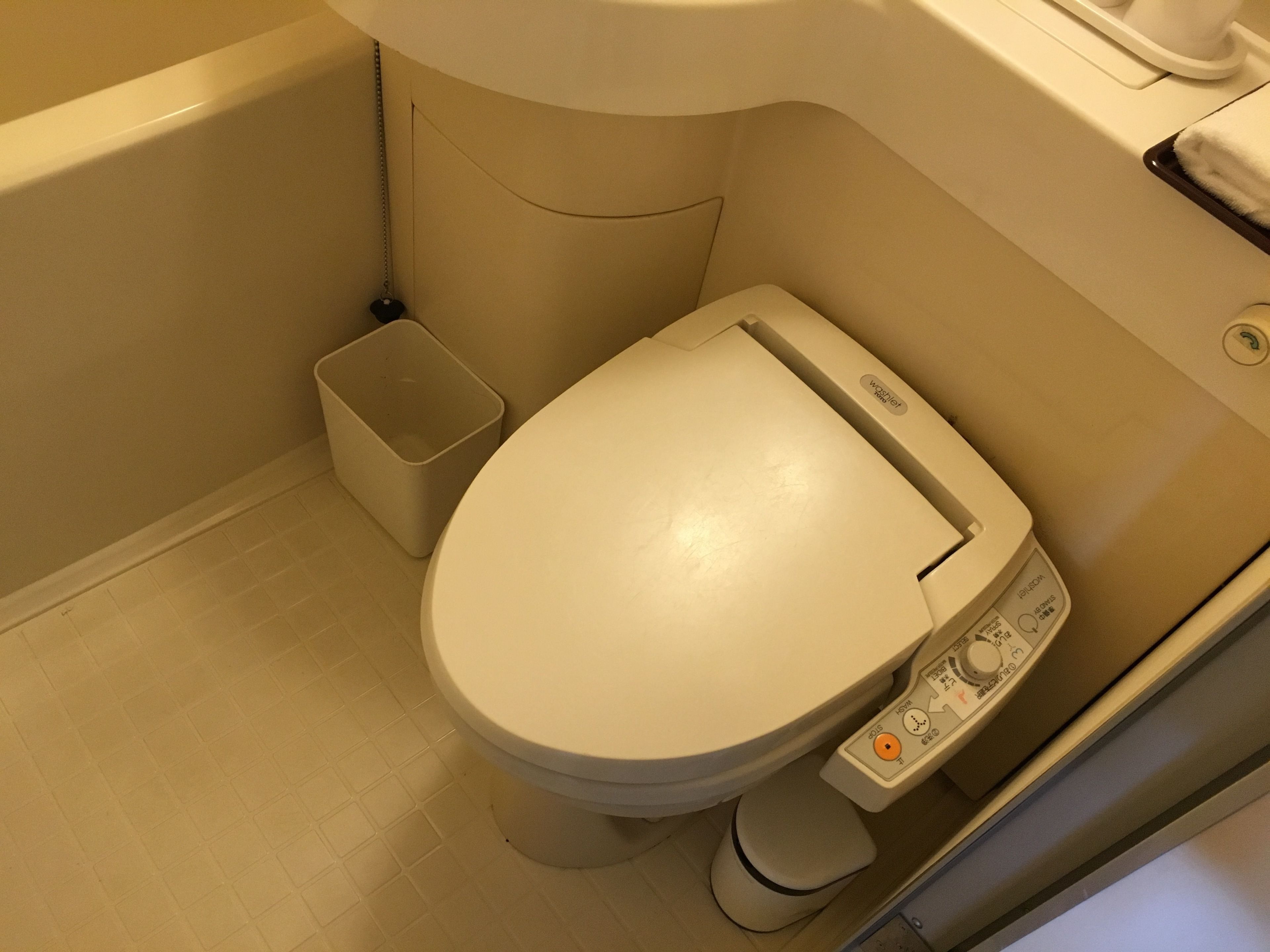 A toilet with a control panel, a small trash bin, and a wall-mounted towel rack.