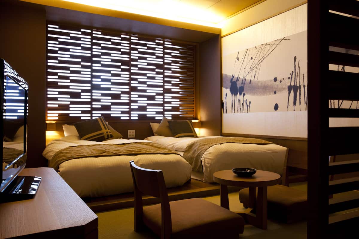 Ein Hotelzimmer mit zwei Betten, einem Schreibtisch, einem Stuhl, einem kleinen Tisch und einem großen, abstrakten Gemälde an der Wand.