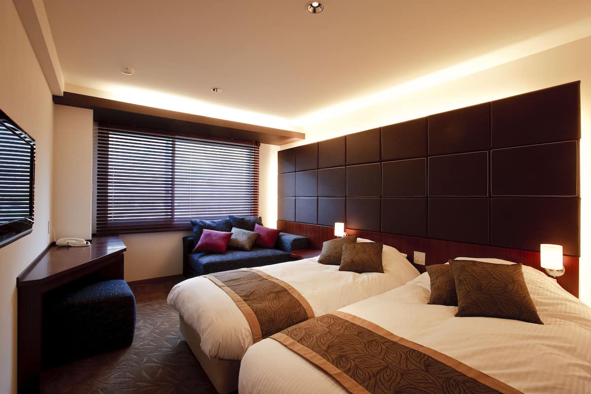 Ein Hotelzimmer mit zwei Betten, einem Schreibtisch und einer Couch.