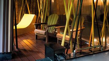 A wooden deck with chairs and bamboo plants, a stone bench, and a glass railing.