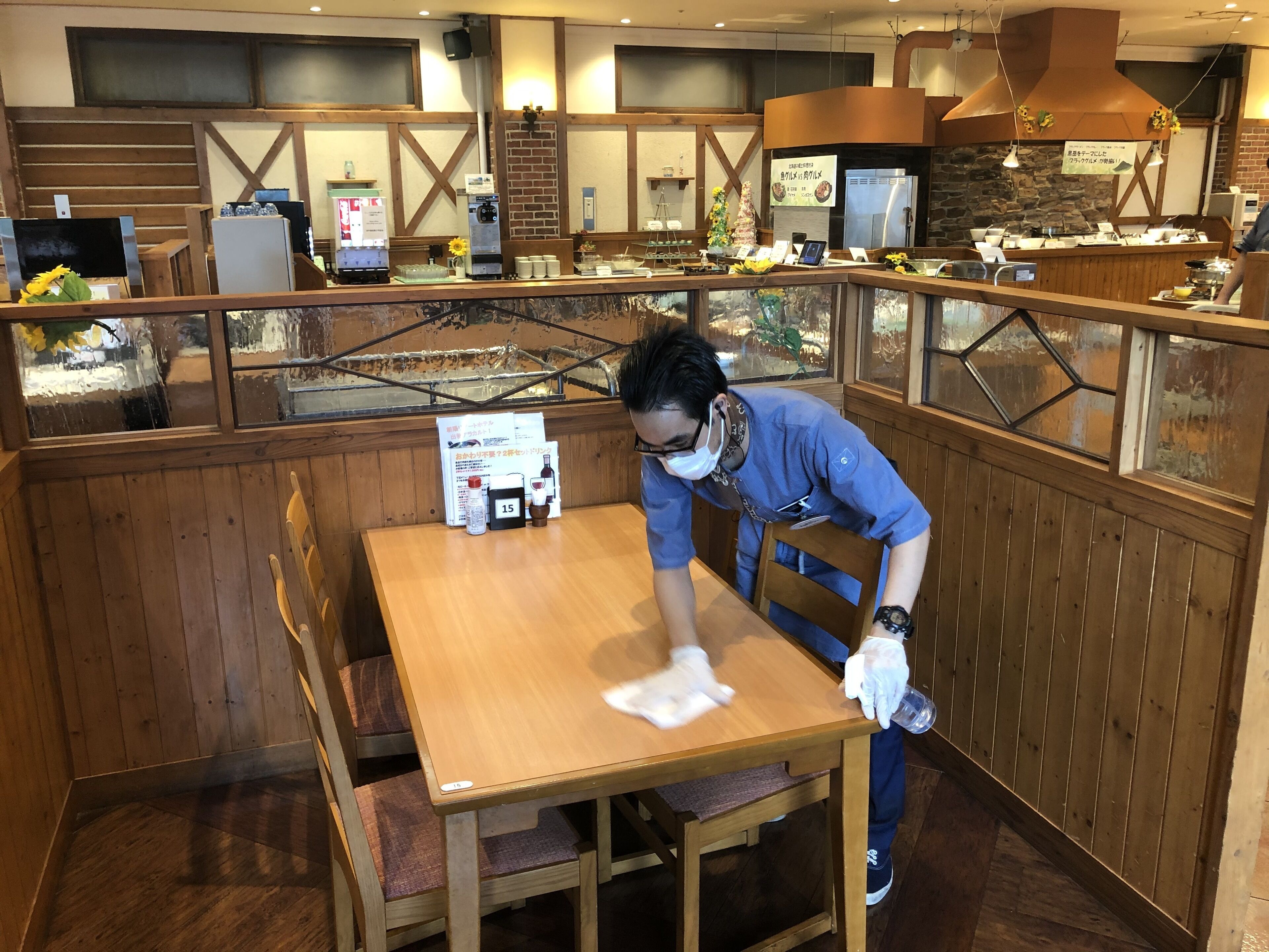 A restaurant interior with wooden furniture, a counter with various items, and a person cleaning a table.