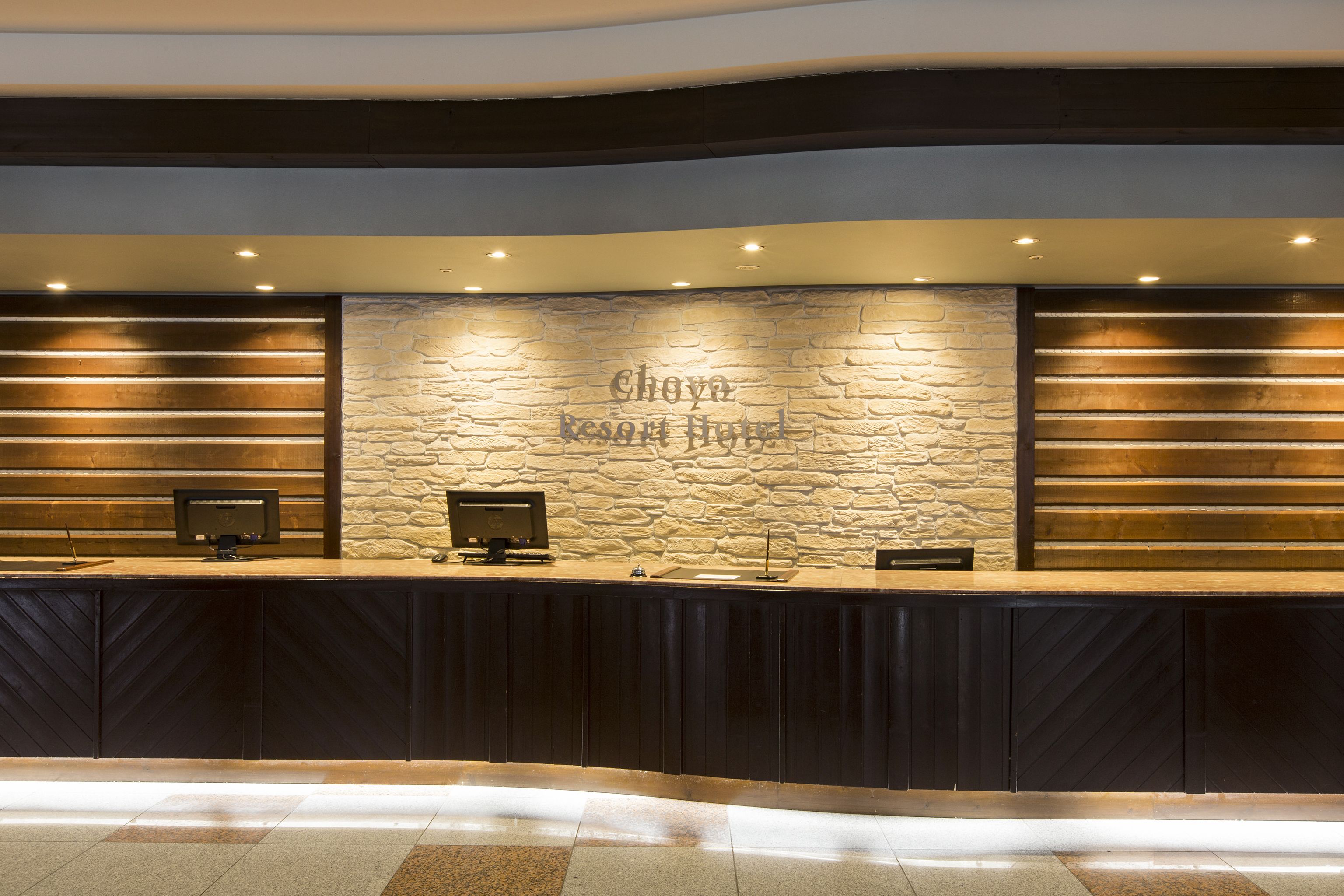 A reception desk with a stone wall backdrop, a wooden bench, and a monitor.