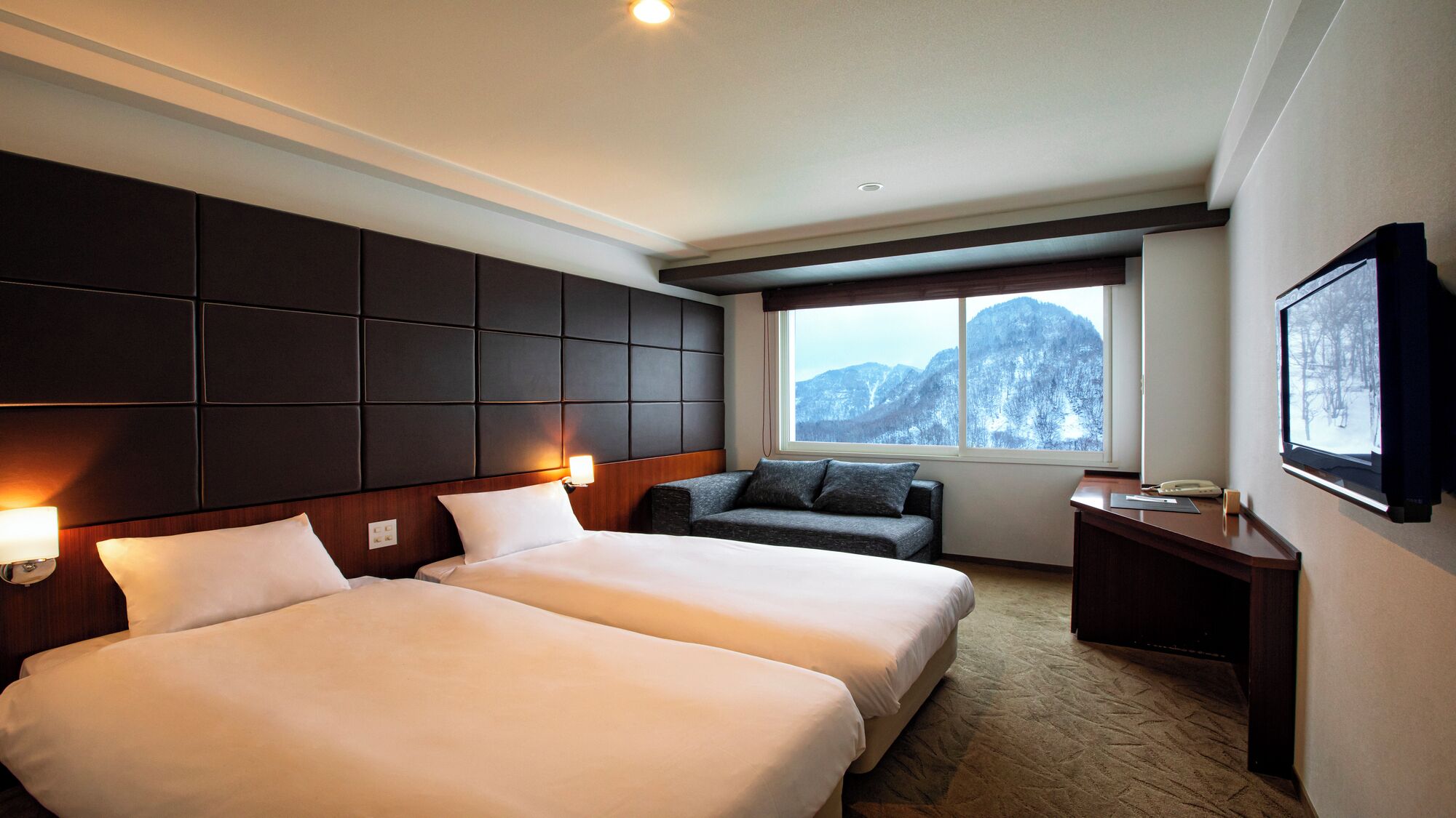 Une chambre d’hôtel avec deux lits, un canapé, un bureau et une grande fenêtre donnant sur la montagne.