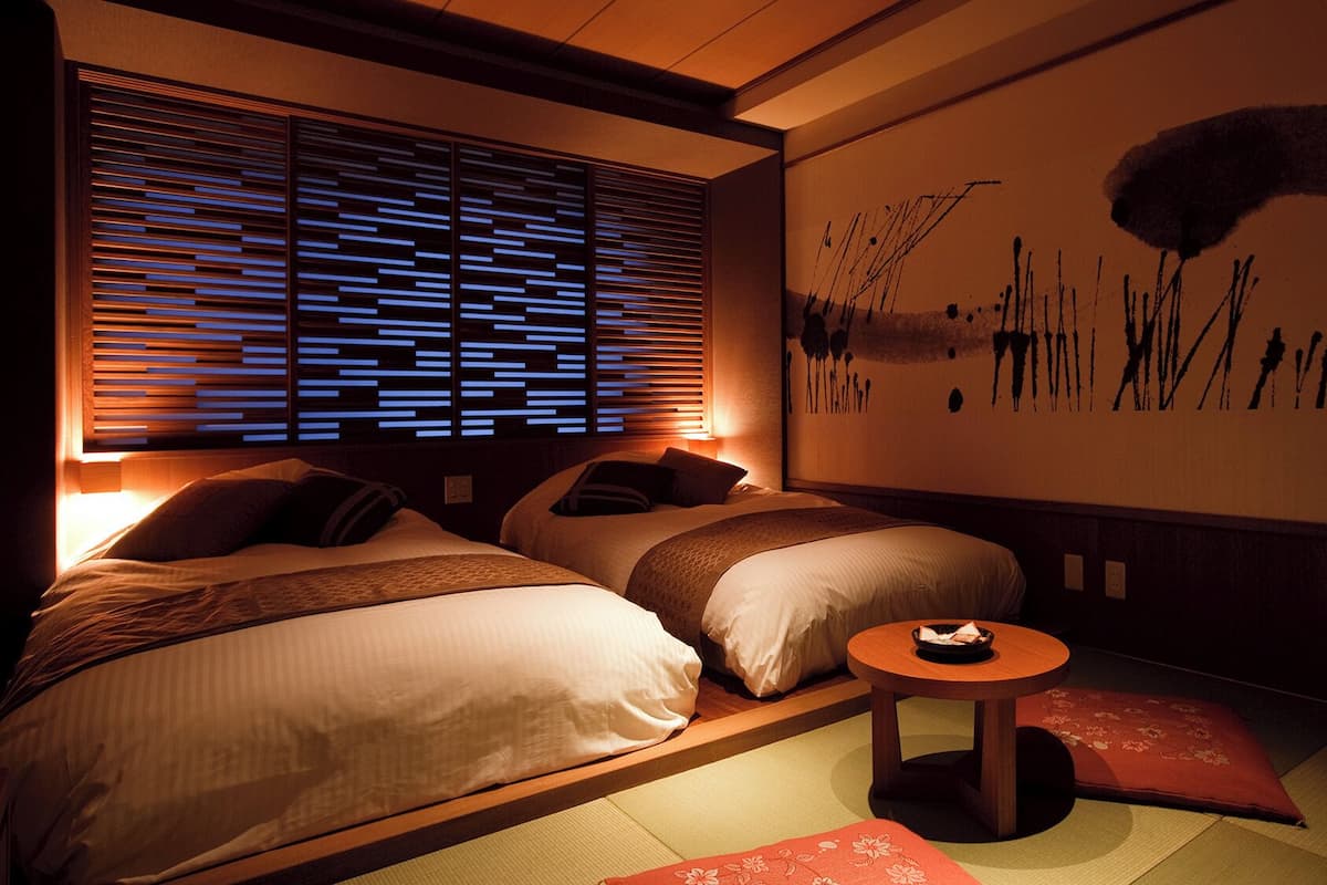 Ein Zimmer mit zwei Betten, einem kleinen runden Tisch und einer Wand mit abstrakter Kunst.