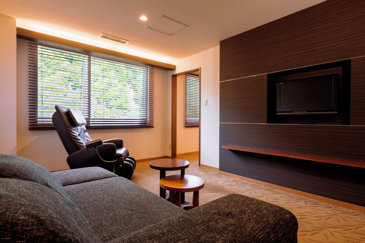 Ein modernes Wohnzimmer mit einer Couch, einem Sessel, einem kleinen Tisch und einem an der Wand befestigten Fernseher.