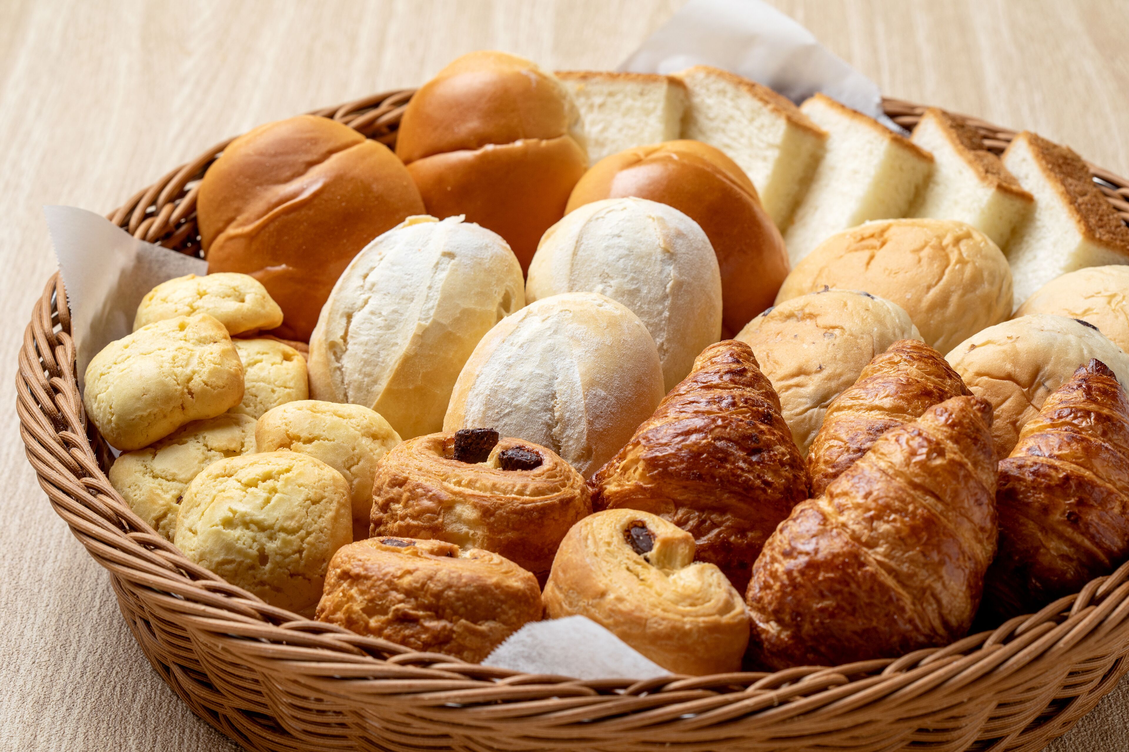 A basket of assorted baked goods including bread, buns, and pastries.