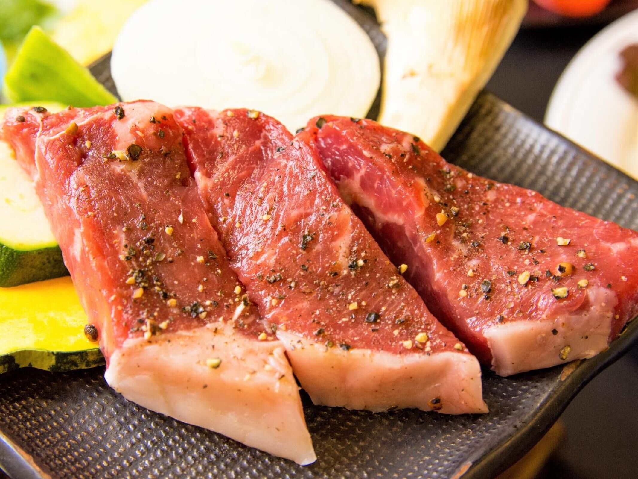 Rohes Fleisch mit Gewürzen, vermutlich zum Kochen gedacht, auf einer strukturierten Platte.