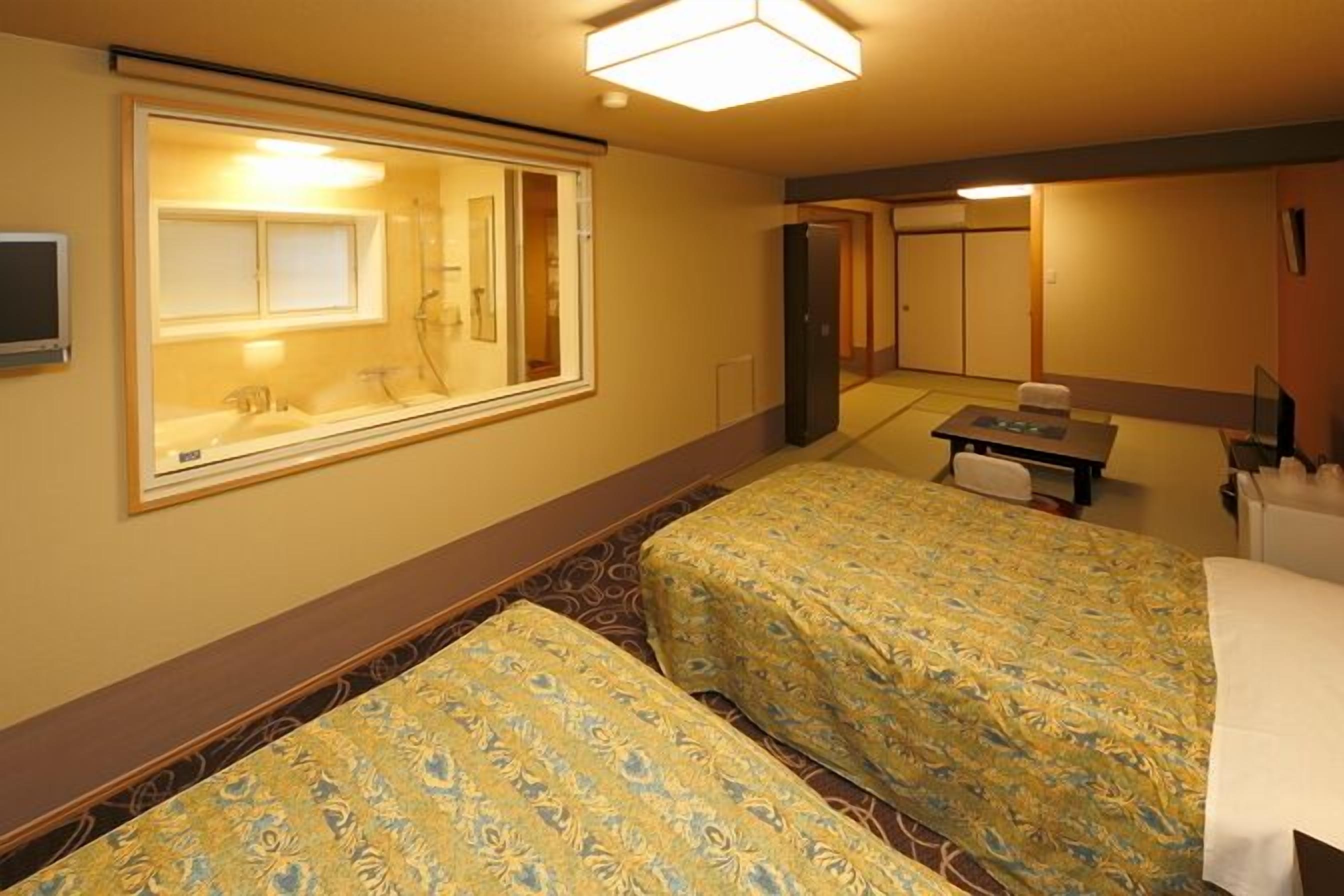 Quarto de hotel com duas camas, uma escrivaninha, uma cadeira, um espelho e uma televisão.
