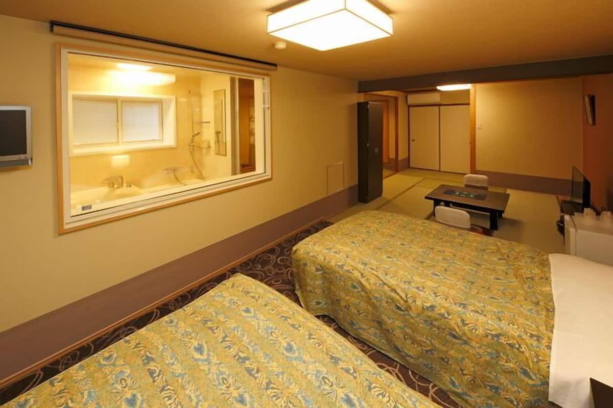 Ett hotellrum med två sängar, ett skrivbord, en stol, en spegel och en tv.