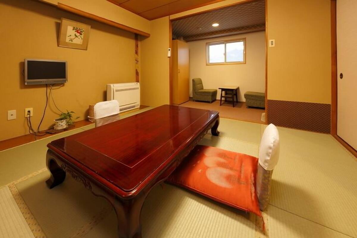 Ein traditioneller Raum mit Tatami-Böden, einem Holztisch, einer Futon-Liege und einem Fernseher.