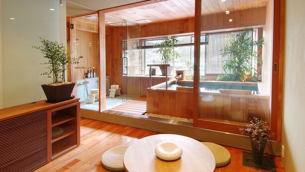 A modern interior with a wooden floor, a round table with a white object, and a large sliding glass door leading to a balcony with plants and a view. - Konpira-spa Yumoto Yachiyo (Kotohira)