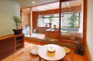 A modern interior with a wooden floor, a round table with a white object, and a large sliding glass door leading to a balcony with plants and a view. - Konpira-spa Yumoto Yachiyo (Kotohira)