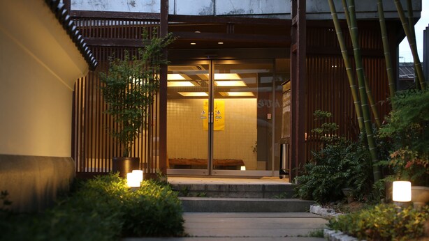 A traditional Japanese building entrance with a wooden gate, a small garden with bamboo, and a pathway leading to the entrance. - Private spa Hotel Kotone (Kotohira)