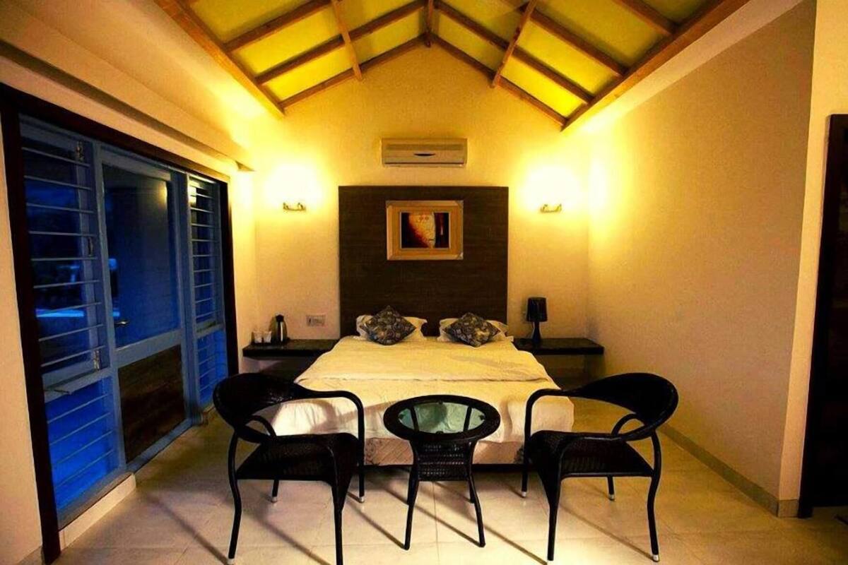 Une chambre à coucher comprenant un lit, deux tables de chevet, une commode, une fenêtre avec des stores et un plafond avec des poutres en bois.