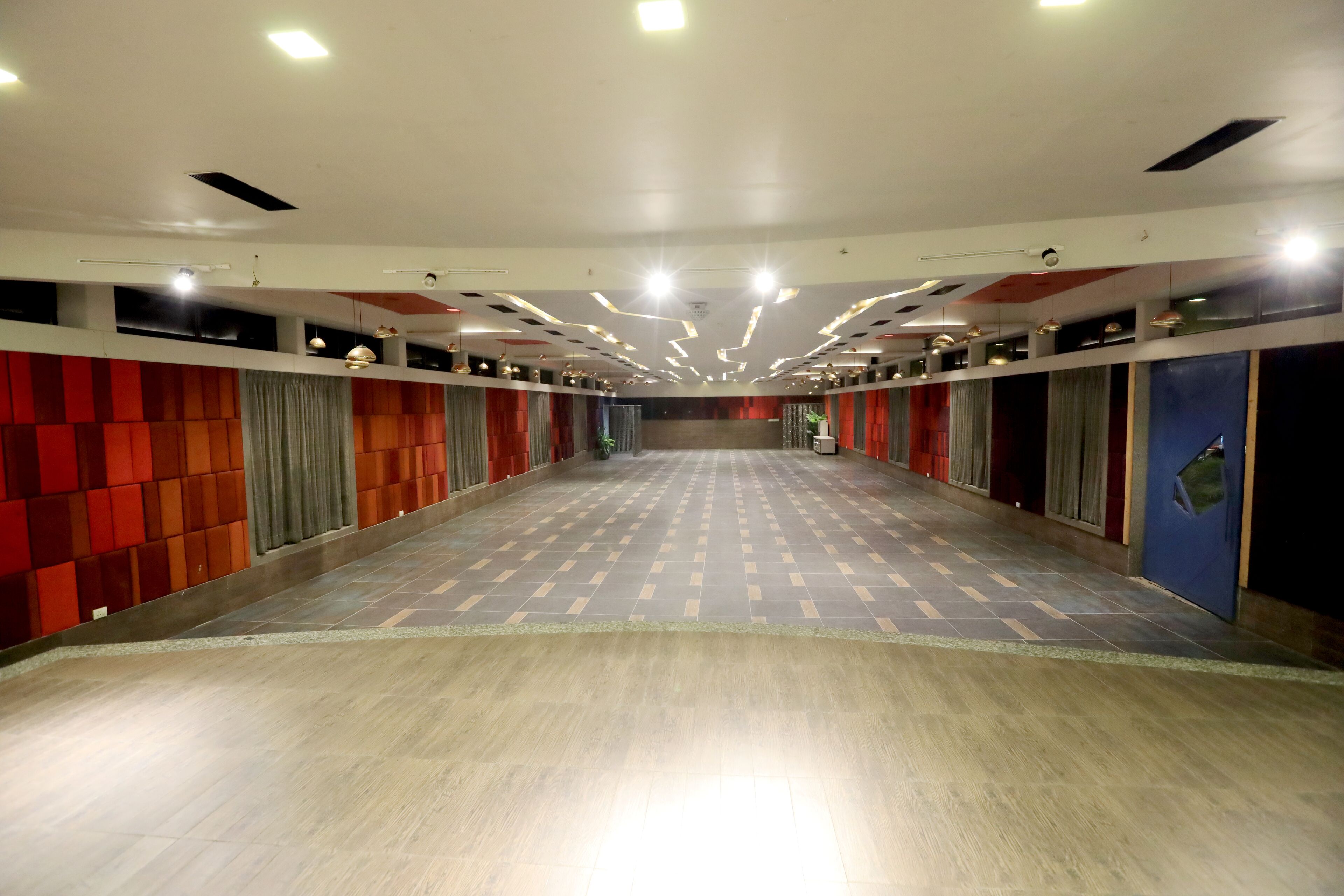 A long corridor with tiled flooring, recessed lighting, and walls with patterned panels.