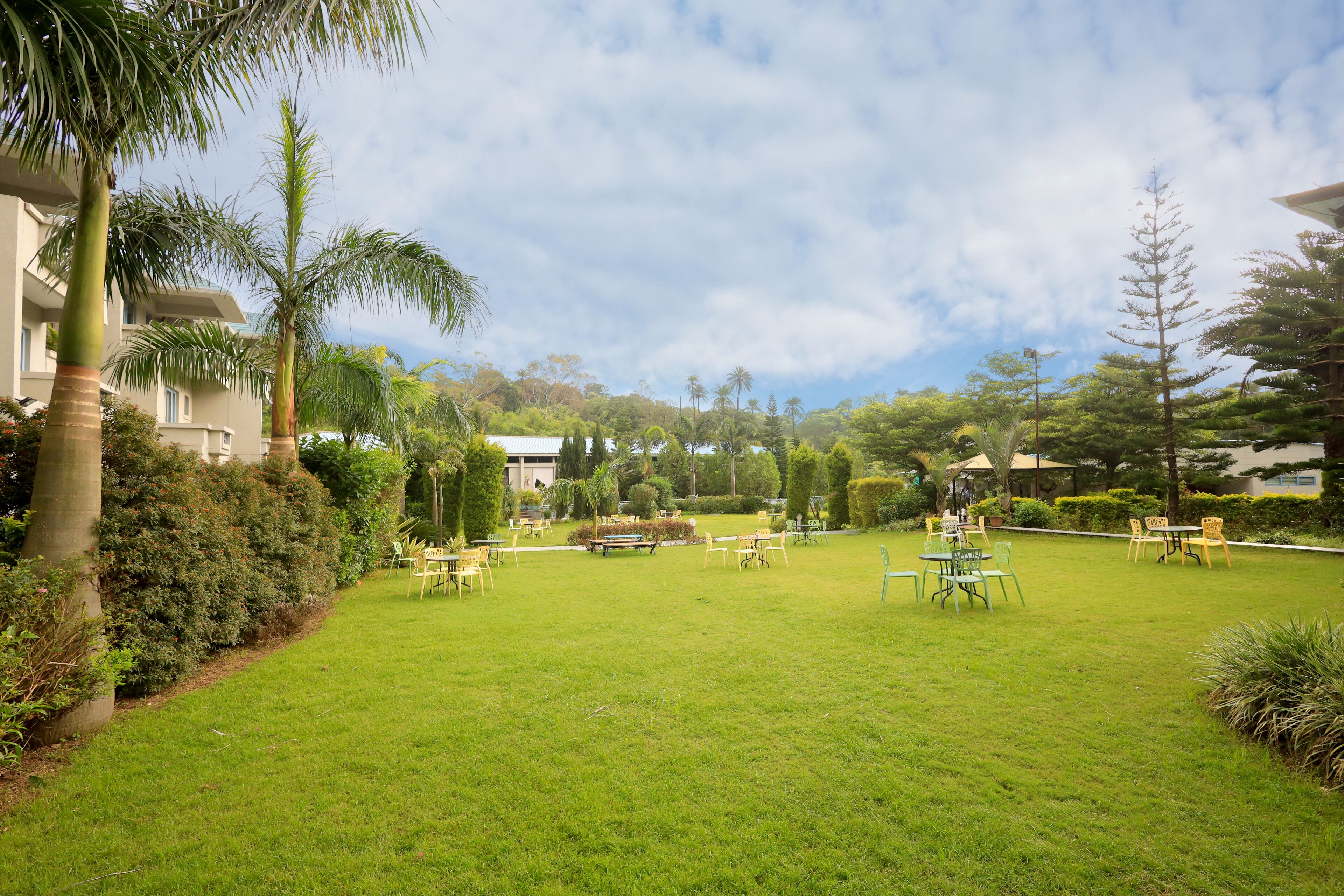 A well-maintained outdoor area with a grassy lawn, several tables and chairs, and a variety of trees and shrubs.