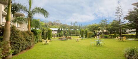A well-maintained outdoor area with a grassy lawn, several tables and chairs, and a variety of trees and shrubs.