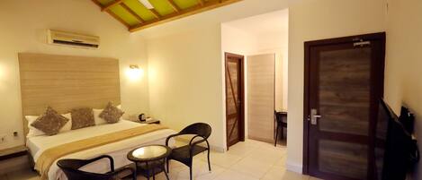 A hotel room with a bed, two chairs, a table, a ceiling fan, an air conditioner, and a TV.