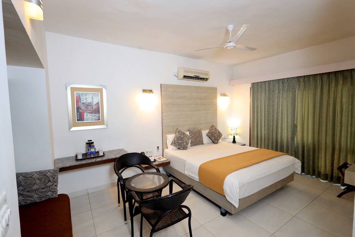 Une chambre d’hôtel avec un lit, un bureau, deux chaises, un ventilateur de plafond et un tableau au mur.