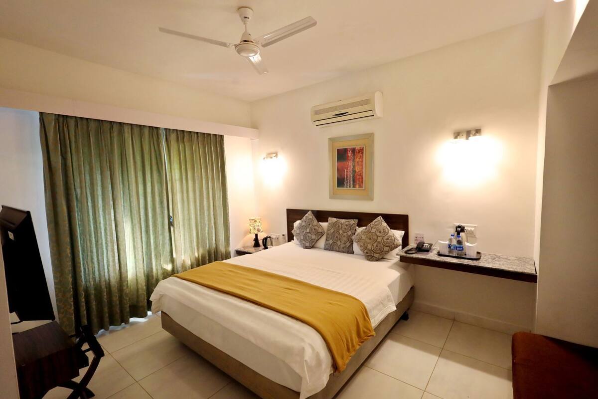 Une chambre d’hôtel équipée d’un lit, d’un bureau, d’une chaise, d’un ventilateur de plafond, d’un climatiseur et d’un tableau au mur.