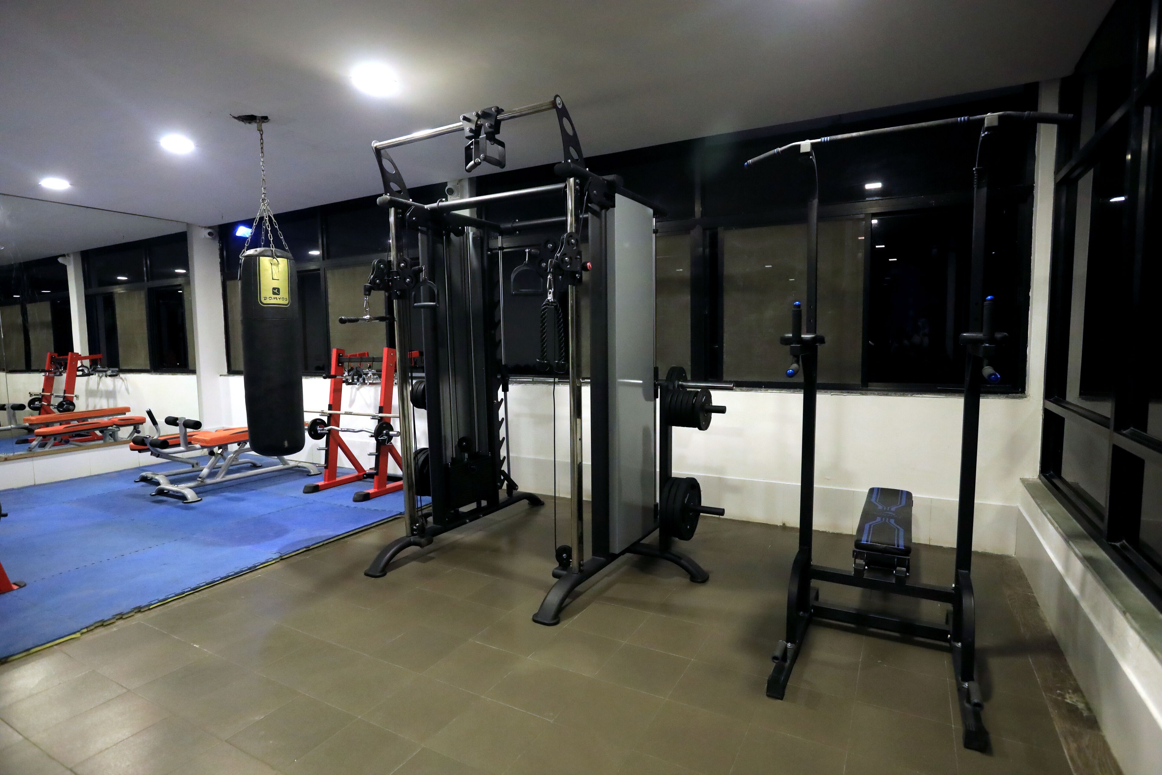 A gym with various exercise equipment, including a squat rack, bench press, and a punching bag.