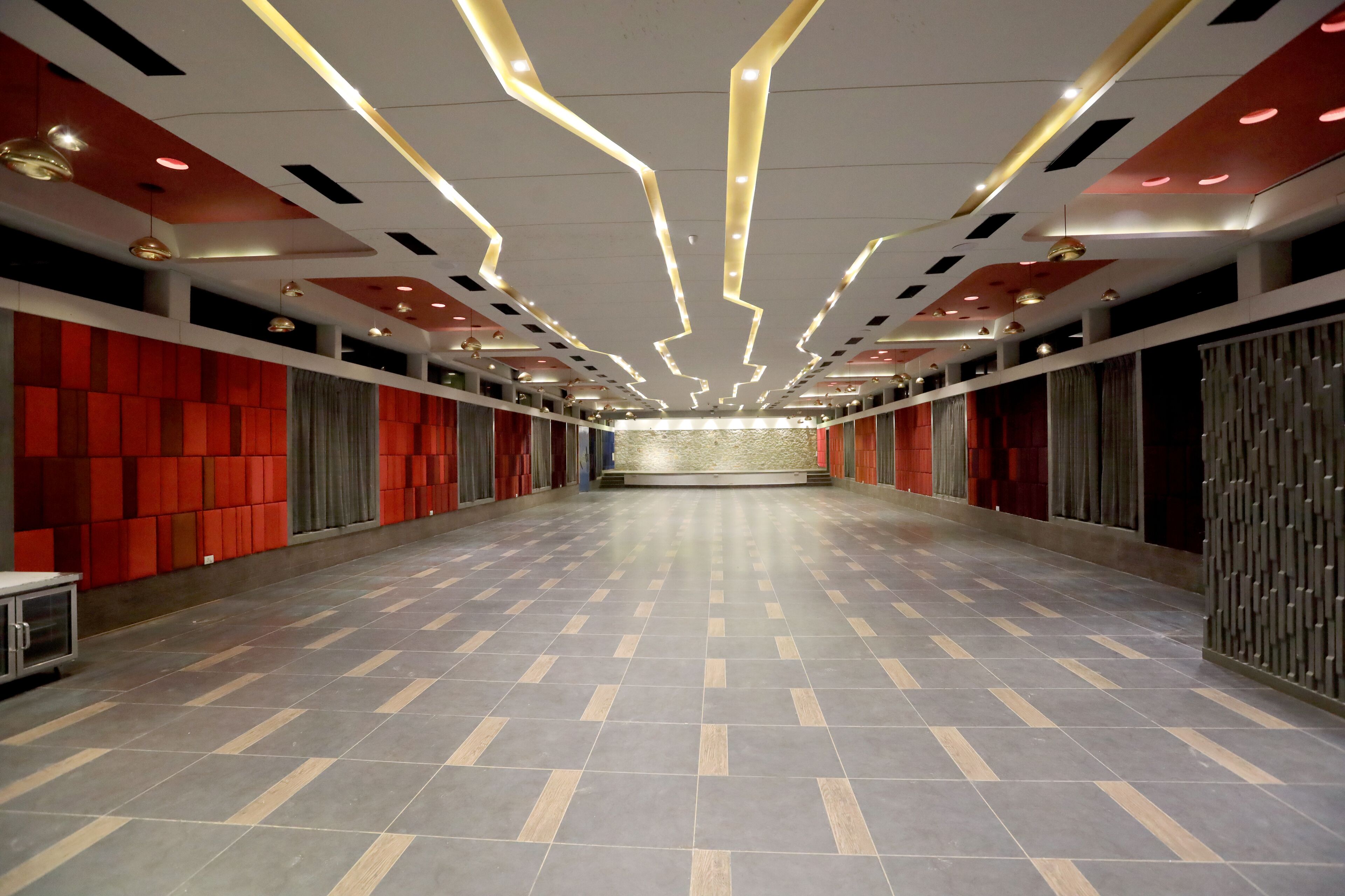 Un vaste couloir d’hôtel doté d’un sol carrelé, de panneaux acoustiques rouges et de luminaires modernes.