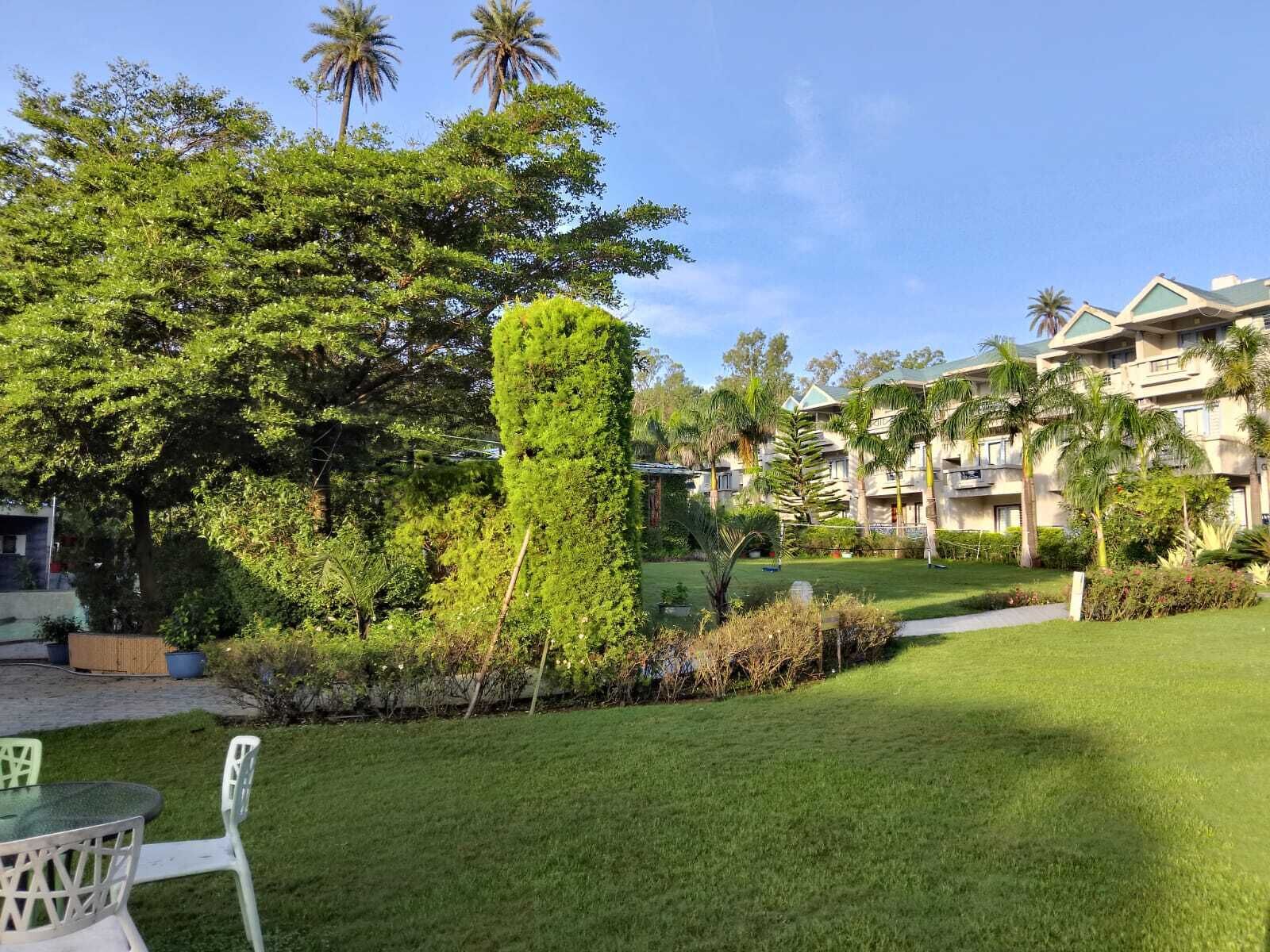 A well-maintained garden with a variety of trees and shrubs, a grassy lawn, and a building with multiple balconies and a modern design.