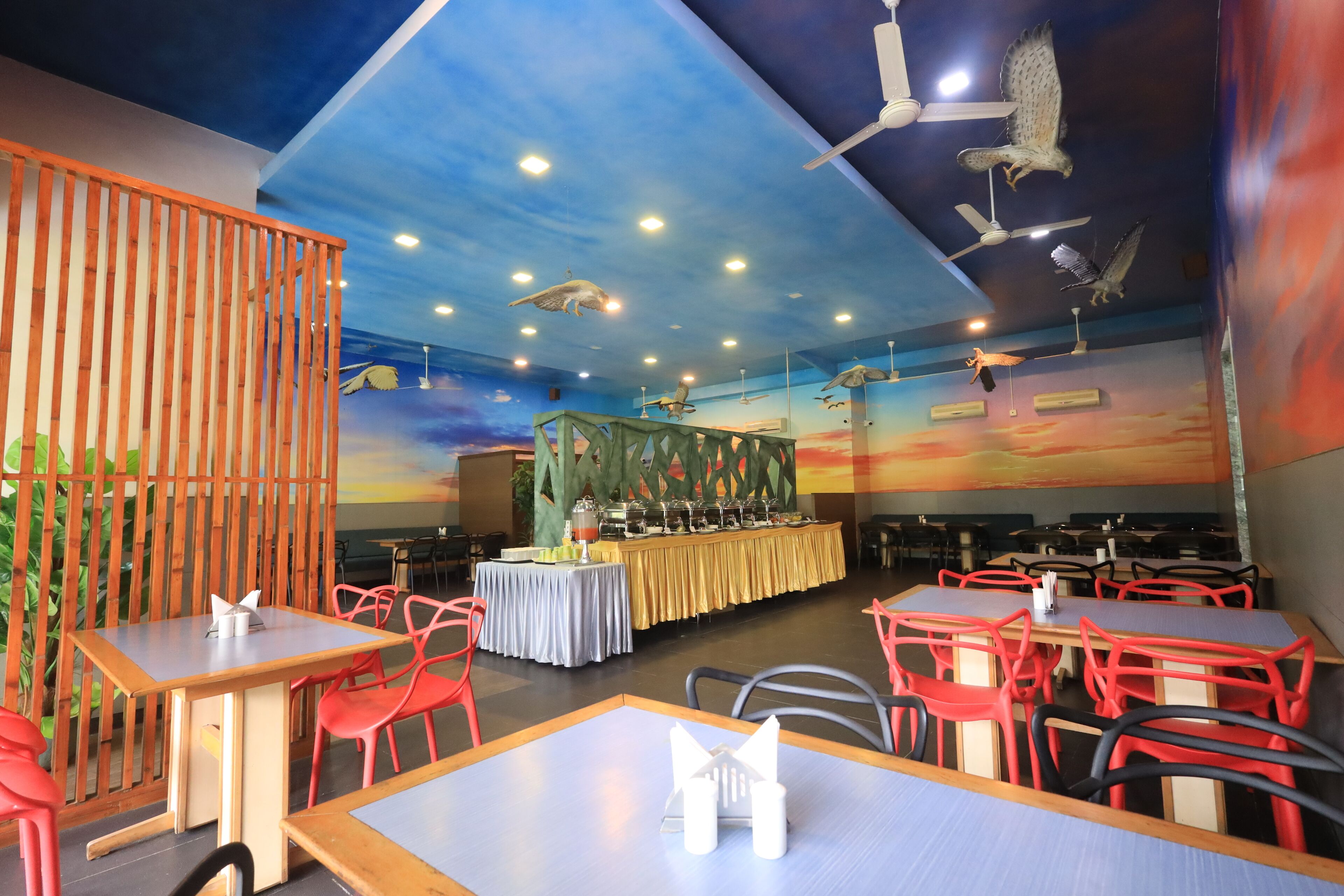 A restaurant with multiple tables and chairs, a buffet setup, and ceiling fans.