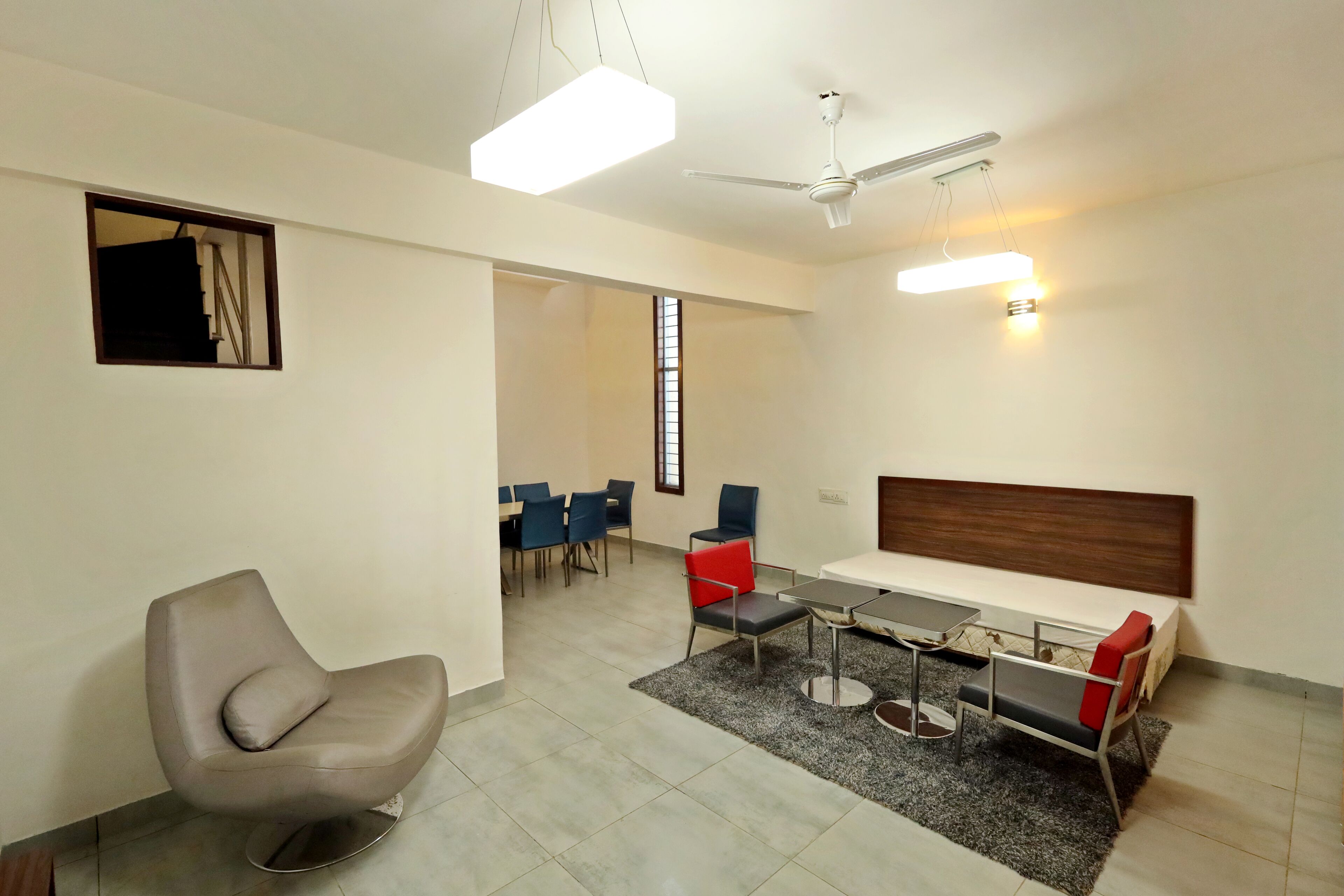 A modern hotel room with a sofa, dining table, chairs, and a ceiling fan.
