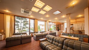 A spacious hotel lobby with leather sofas, a wooden coffee table, and large windows offering a view of the outdoors. - Beachside Hotel Kashimaso (Tonosho)