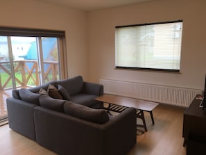 A living room with a grey sofa, a wooden coffee table, and a window with blinds. - Ume House (Furano)