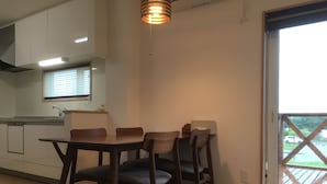 A dining area with a table and chairs, a window with blinds, and a view of a deck outside. - Ume House (Furano)