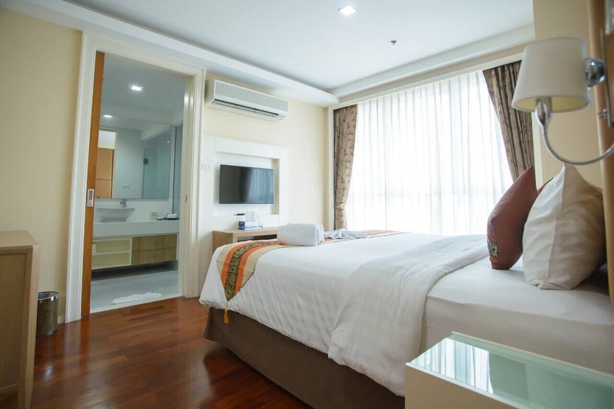 Habitación de hotel con una cama grande, televisión, baño con espejo y ventana con cortinas.