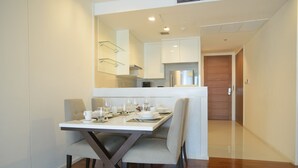 A dining area with a table set for four, a kitchen in the background, and a wooden door leading to another room.