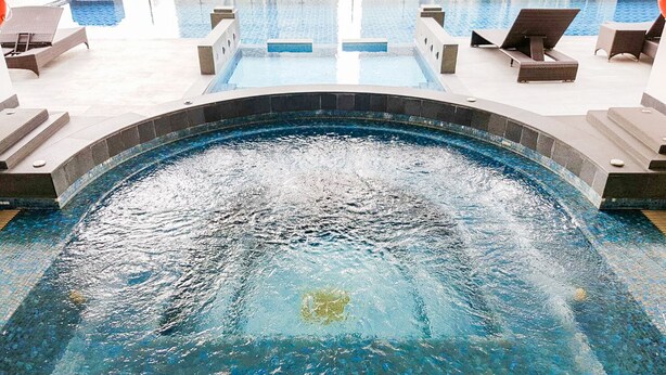 A swimming pool with a water fountain feature, surrounded by lounge chairs and a tiled deck.