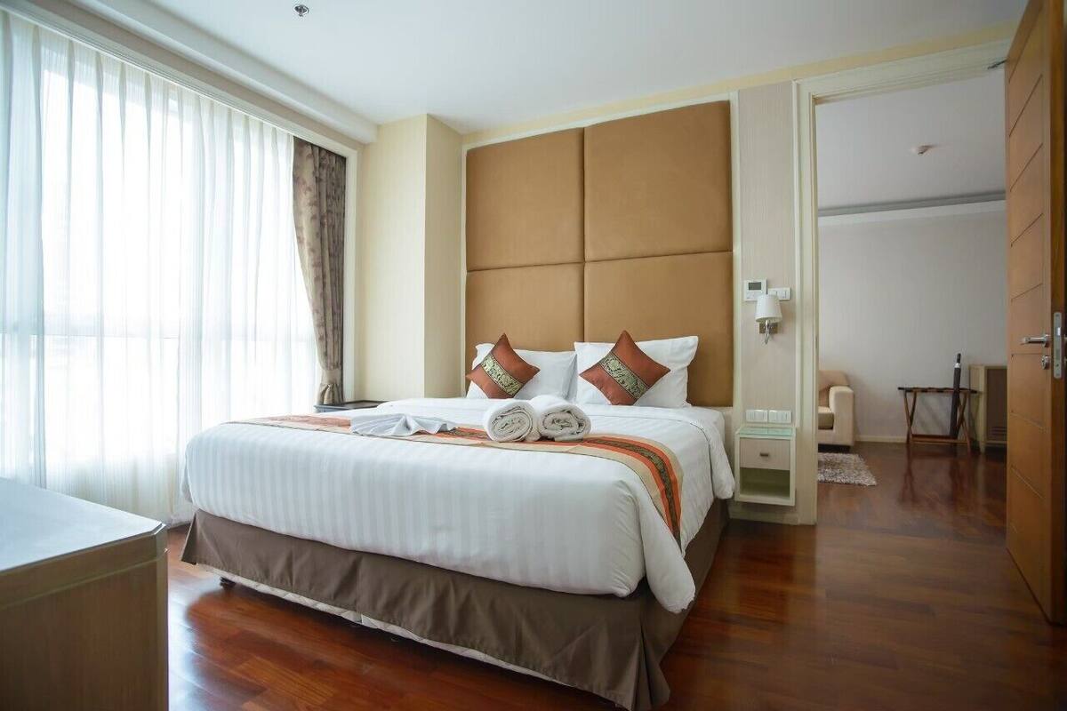 Habitación de hotel con una cama grande, una mesita de noche, una lámpara y vistas al exterior por la ventana.