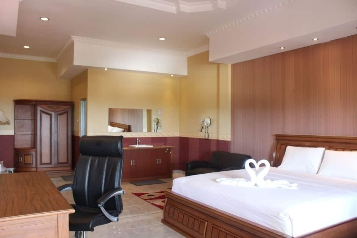 Ein Hotelzimmer mit einem großen Bett, einem Holztisch, einem Ledersessel, einem Frisiertisch mit Spiegel und einem Holzschrank.