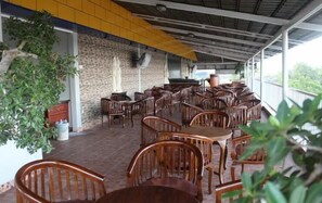 Un café al aire libre con mesas y sillas de madera, paredes de piedra y techo amarillo.