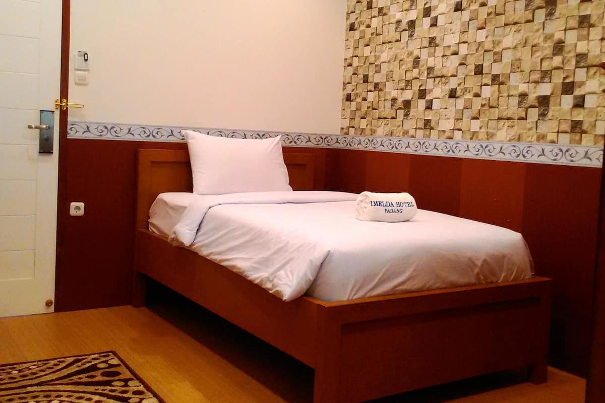 Ein Einzelbett mit weißer Bettdecke und Kissen, ein Holz-Kopfteil, ein gemustertes Teppich und eine Wand mit Mosaikmuster sowie ein Gemälde über dem Bett.