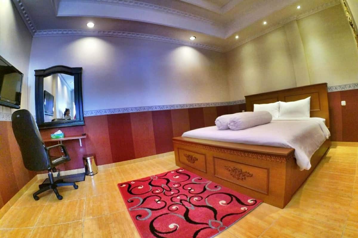 Ein Hotelzimmer mit einem Bett, einem Schreibtisch mit Stuhl, einem Spiegel und einem roten Teppich mit Muster.
