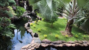 Ein friedlicher Garten mit Teich, Steinen und verschiedenen Pflanzen.