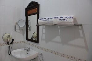 Un baño con un lavamanos blanco, un espejo, un secador de pelo y dos toallas con la inscripción "IMELDA HOTEL PADANG".