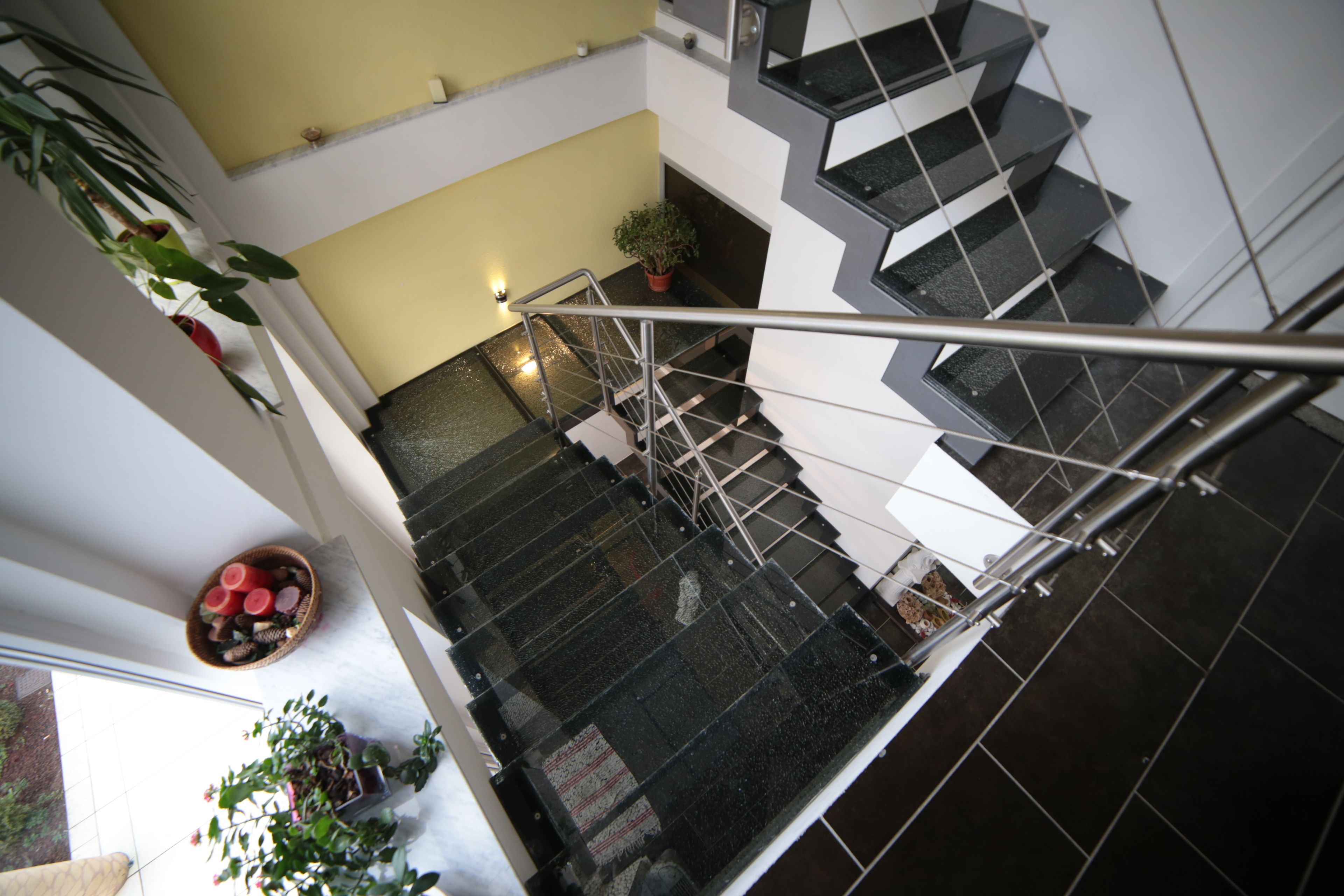 A modern interior with a glass staircase, potted plants, and a bowl of fruit on the landing.