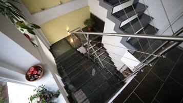 A modern interior with a glass staircase, potted plants, and a bowl of fruit on the landing.