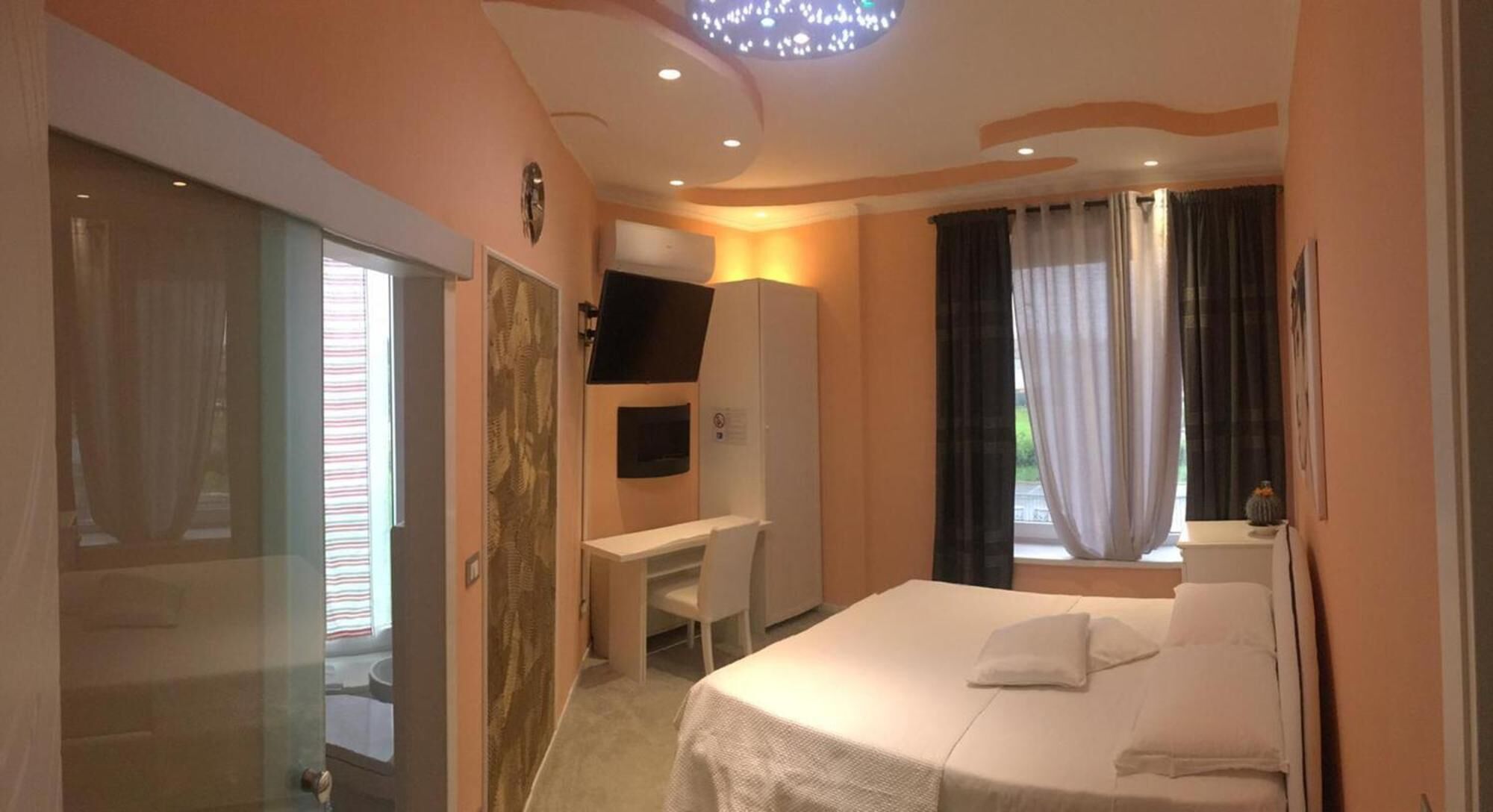 Una habitación de hotel con cama, escritorio, silla, televisión y ventana con cortinas.