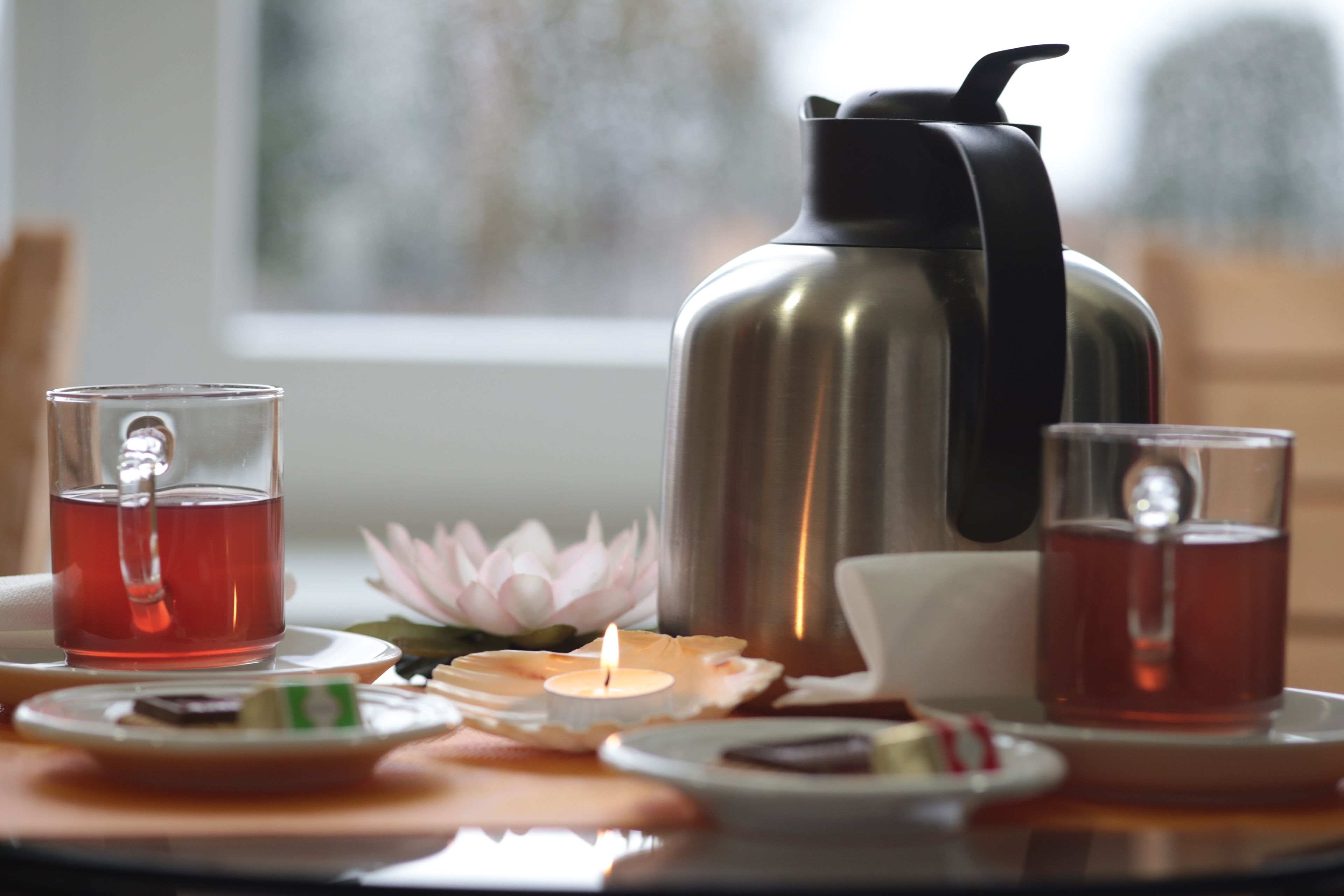 Una mesa con un juego de té, una termo, una vela y una flor de loto.