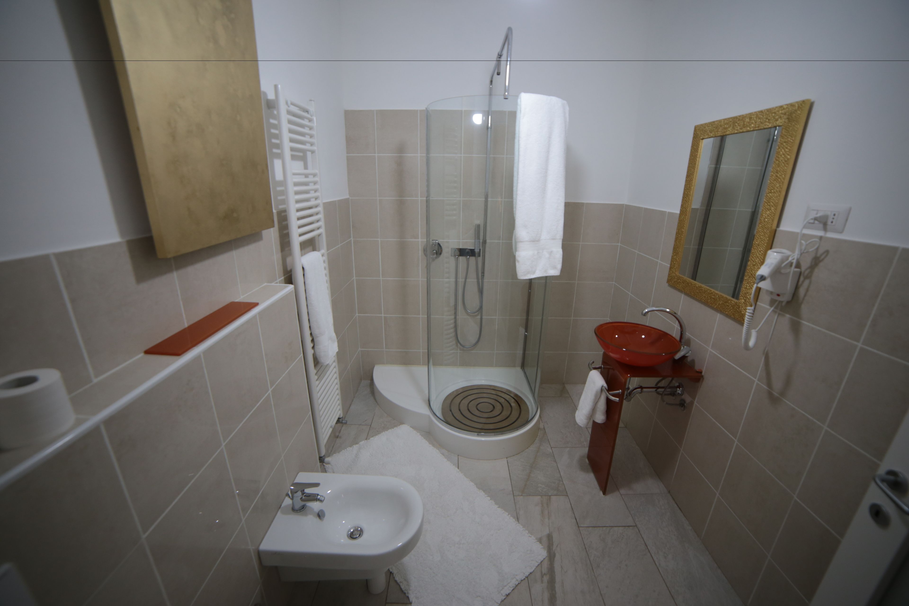 A compact bathroom with a glass-enclosed shower, a pedestal sink, and a vanity with a mirror.