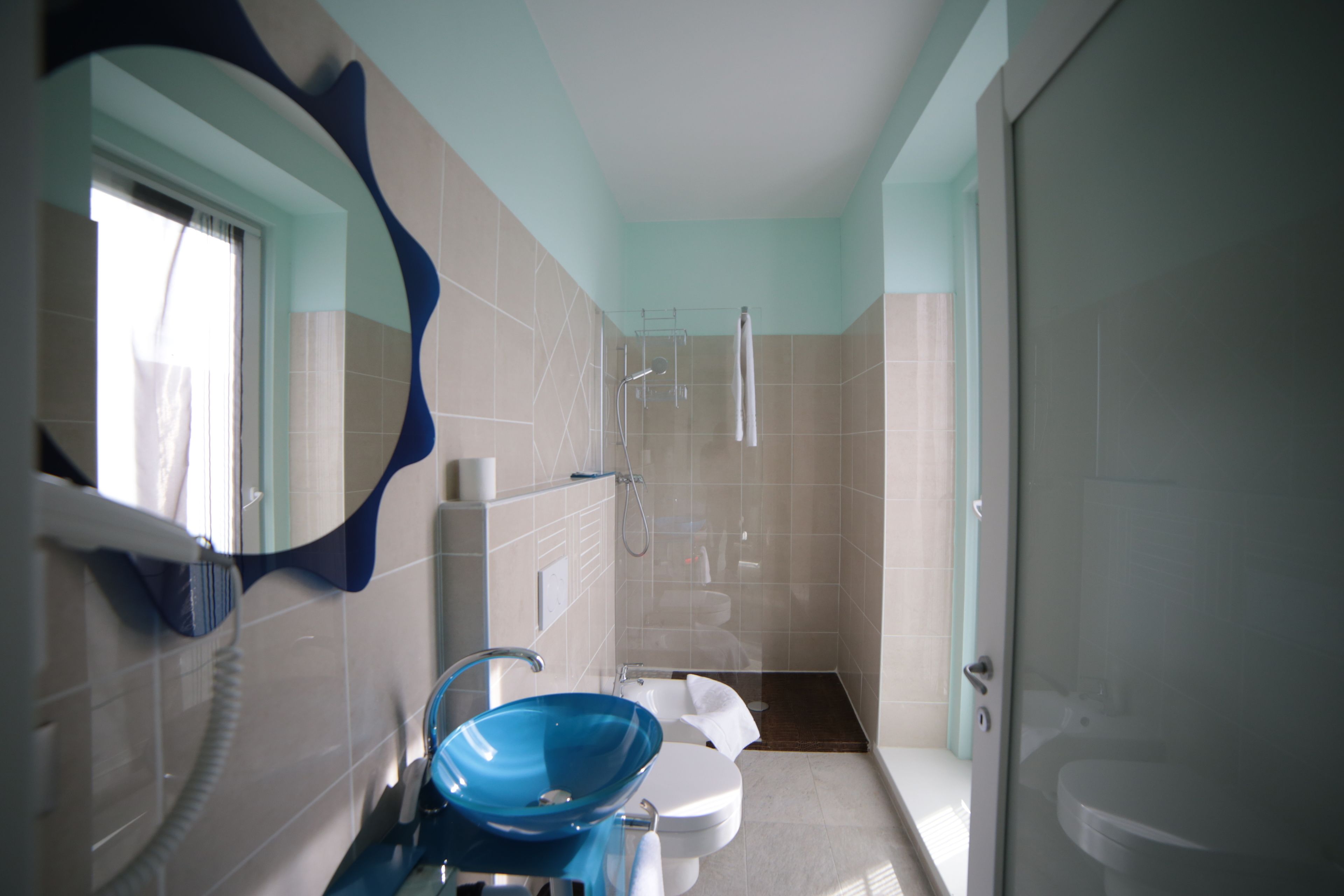 A bathroom with a blue vessel sink, a toilet, a shower, and a mirror with a blue frame.