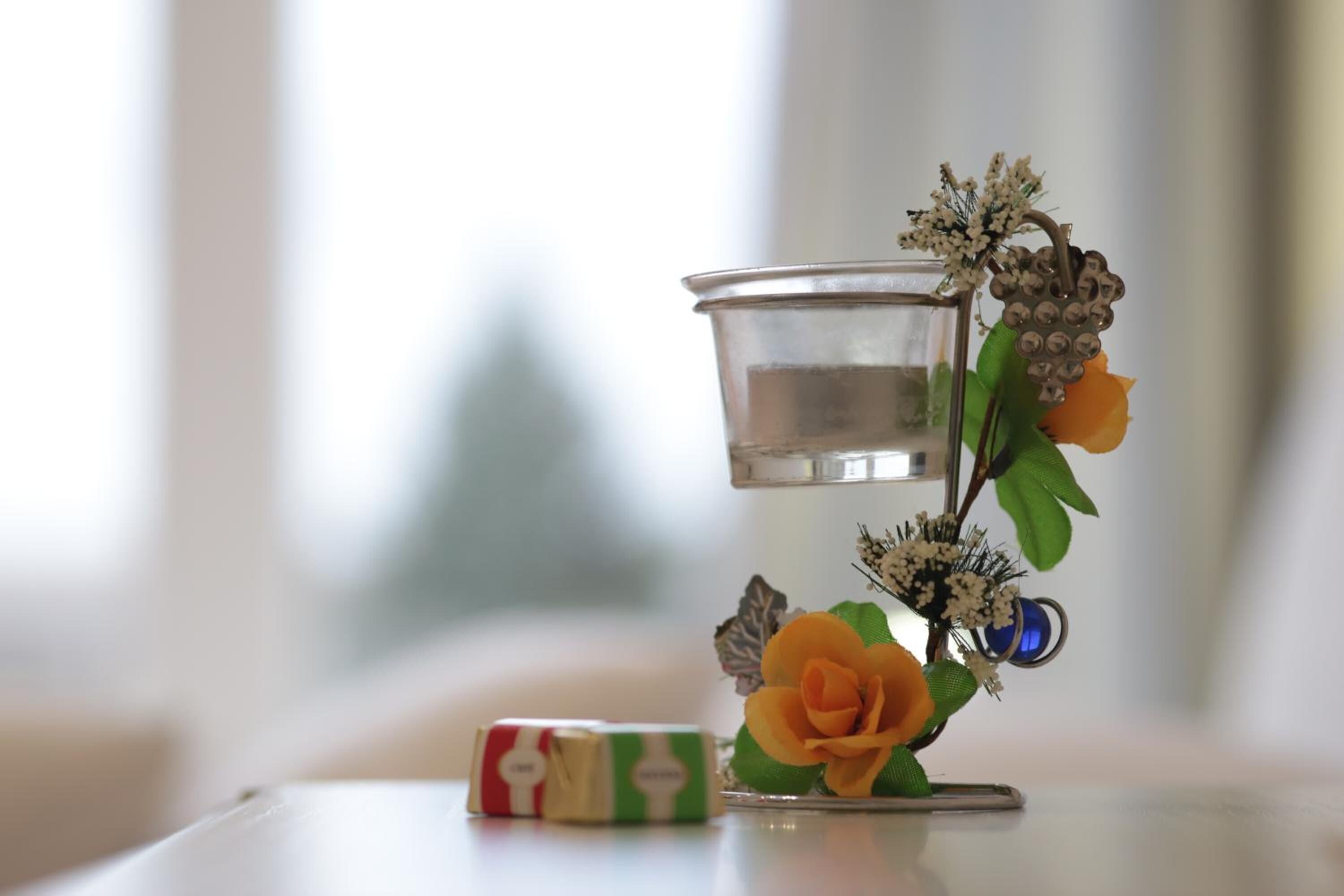A candle holder with a clear glass container, a yellow flower, and a decorative metal piece.