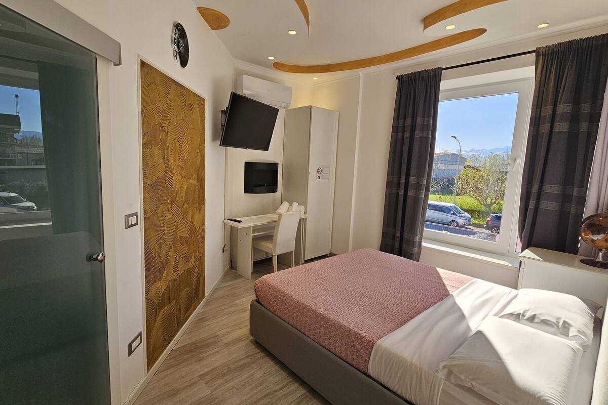 A hotel room with a bed, a desk, a TV, and a window with curtains.